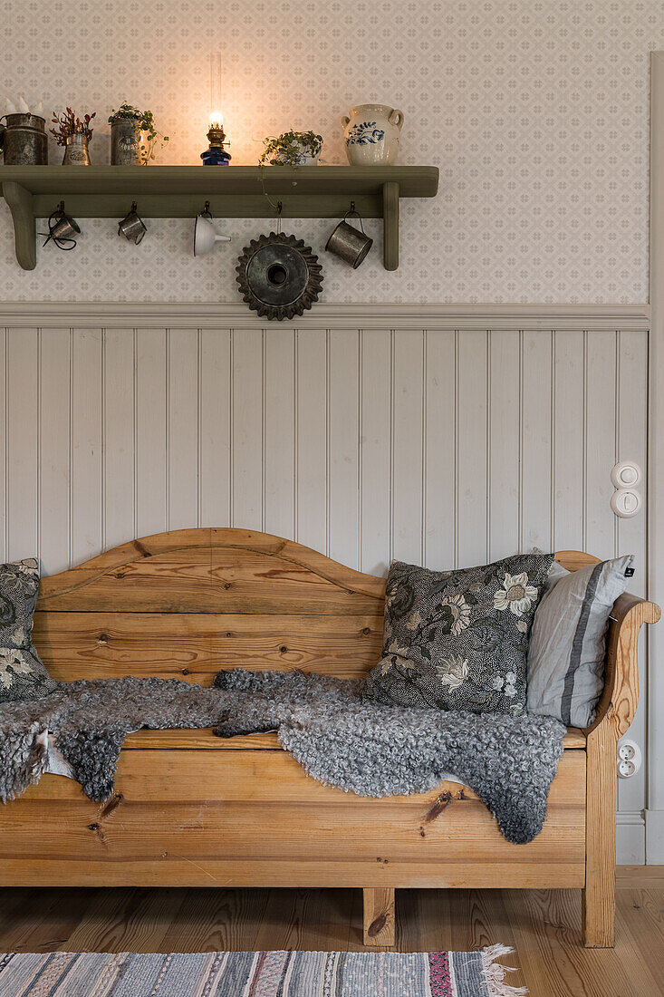 Holzsofa mit Tierfell und Kissen vor Holzverkleideter Wand, darüber Regal mit Vintage Dekoobjekten