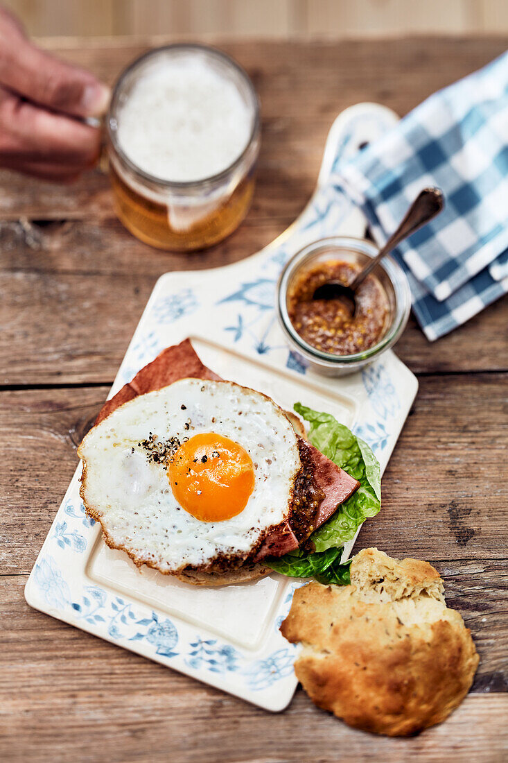 Liver loaf sandwich with a fried egg, served with sweet mustard, and a glass of beer