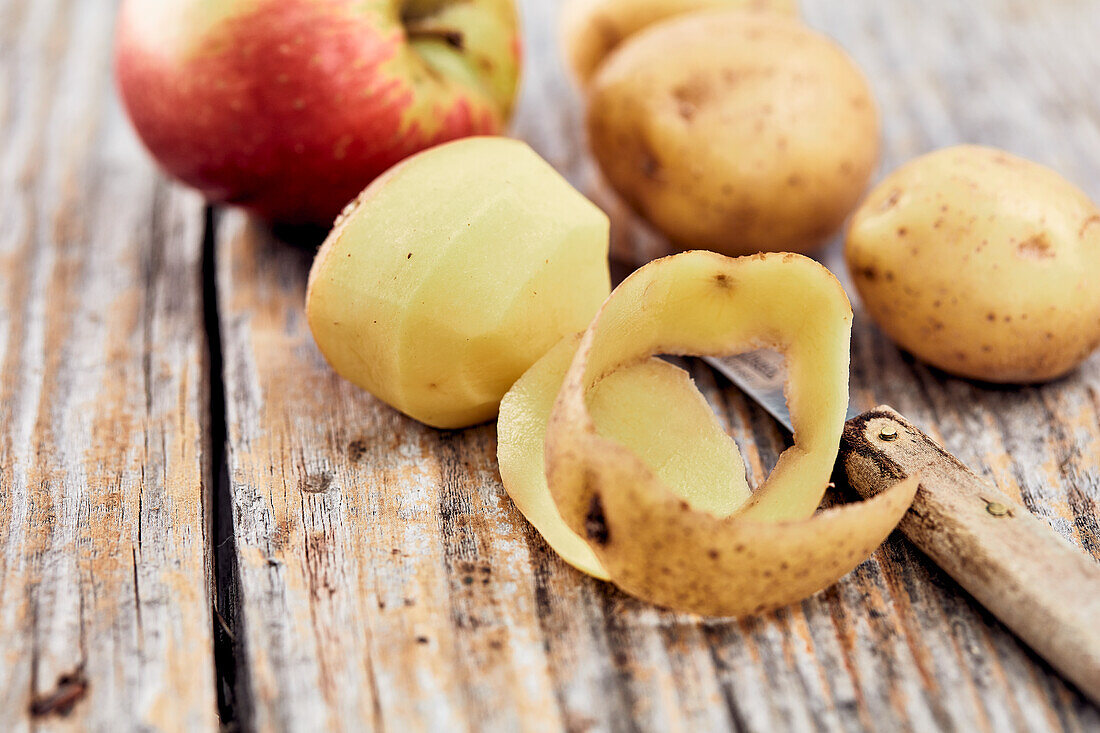 Potatoes, partly peeled and an apple on a wooden table top