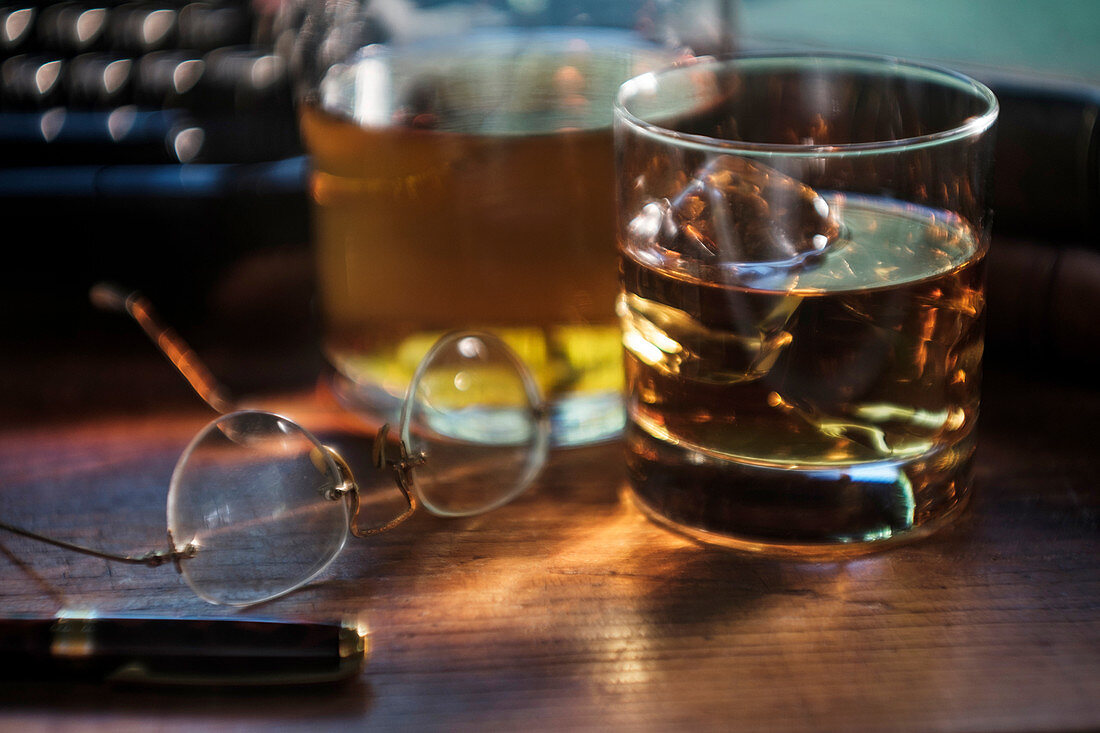 Whiskey glass and eyeglasses next to typewriter on desk