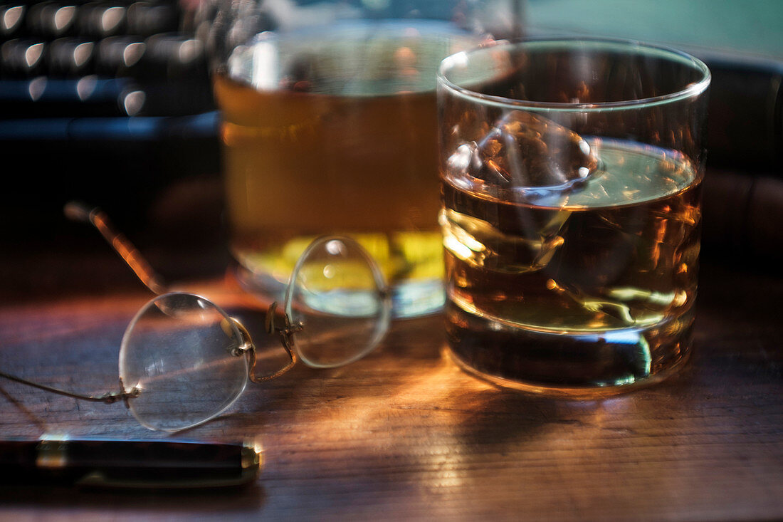 Whiskyglas und Brille neben Schreibmaschine auf Schreibtisch