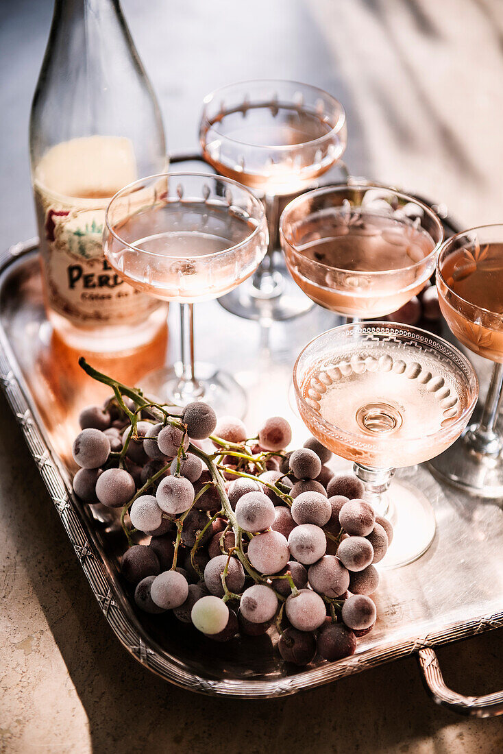 Roséwein in Gläsern und gefrorene Trauben auf Tablett