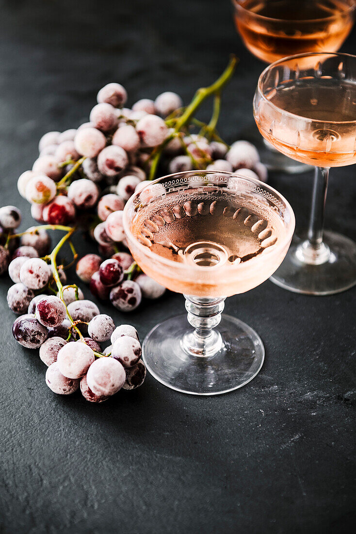 Roséwein in Gläsern daneben gefrorene Trauben