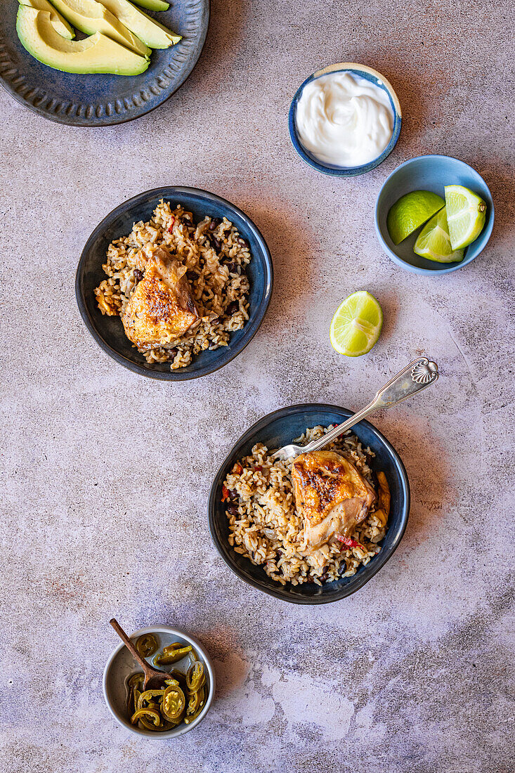 Reis mit Hähnchenoberkeulen (One Pot) serviert mit Chilis, Avocado und Limetten