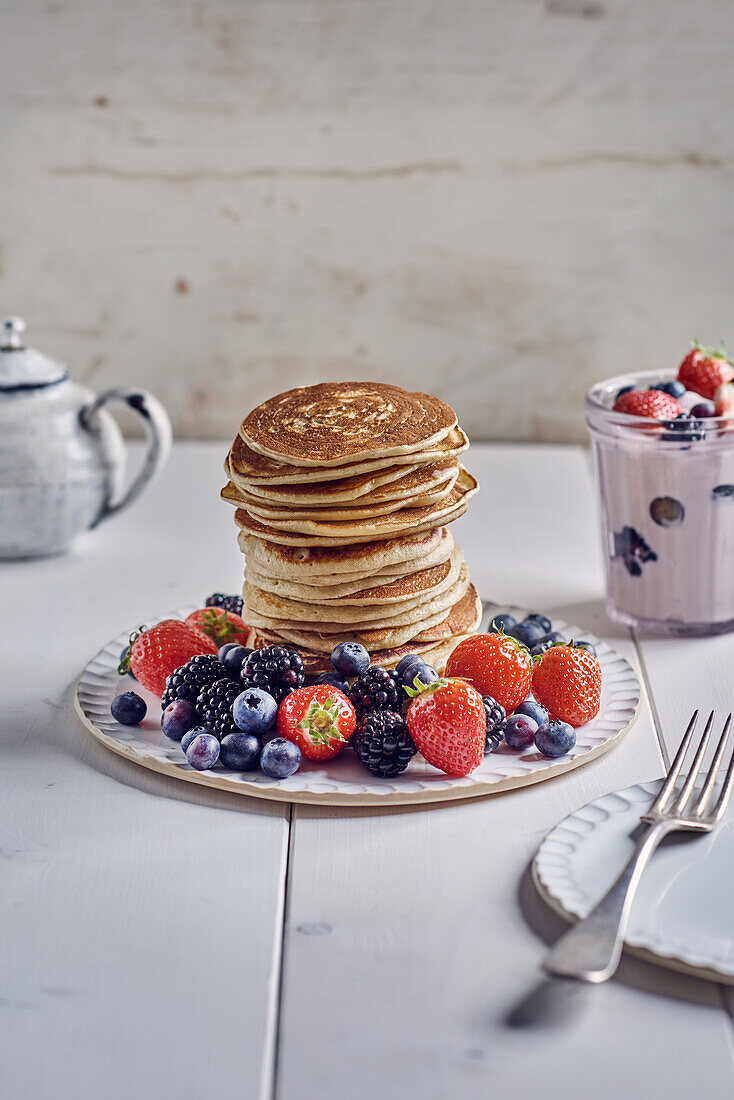 A stack of pancakes with fresh berries and strawberry yogurt