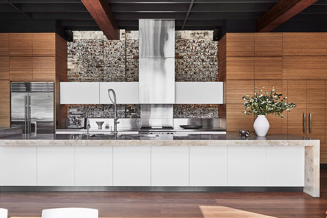 Long kitchen island with concrete slab and wooden cabinets in an open kitchen