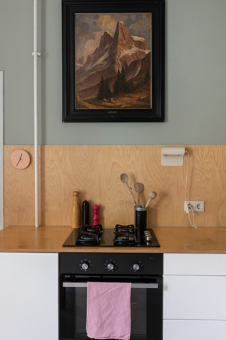 Kitchen counter with gas cooker below wooden splashback and vintage painting