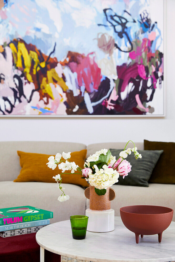 Blick über Marmor-Coffeetable mit Blume auf Sofa mit Kissen, darüber Kunstwerk