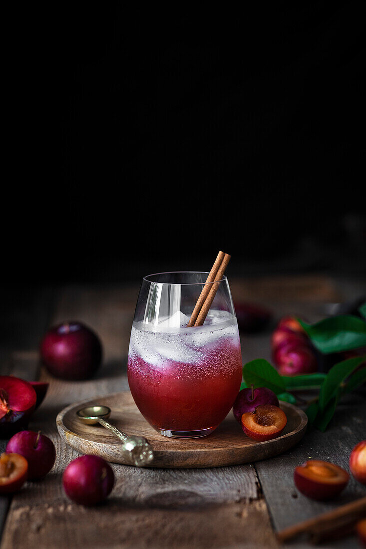 A plum shrub cocktail surrounded by fresh plums