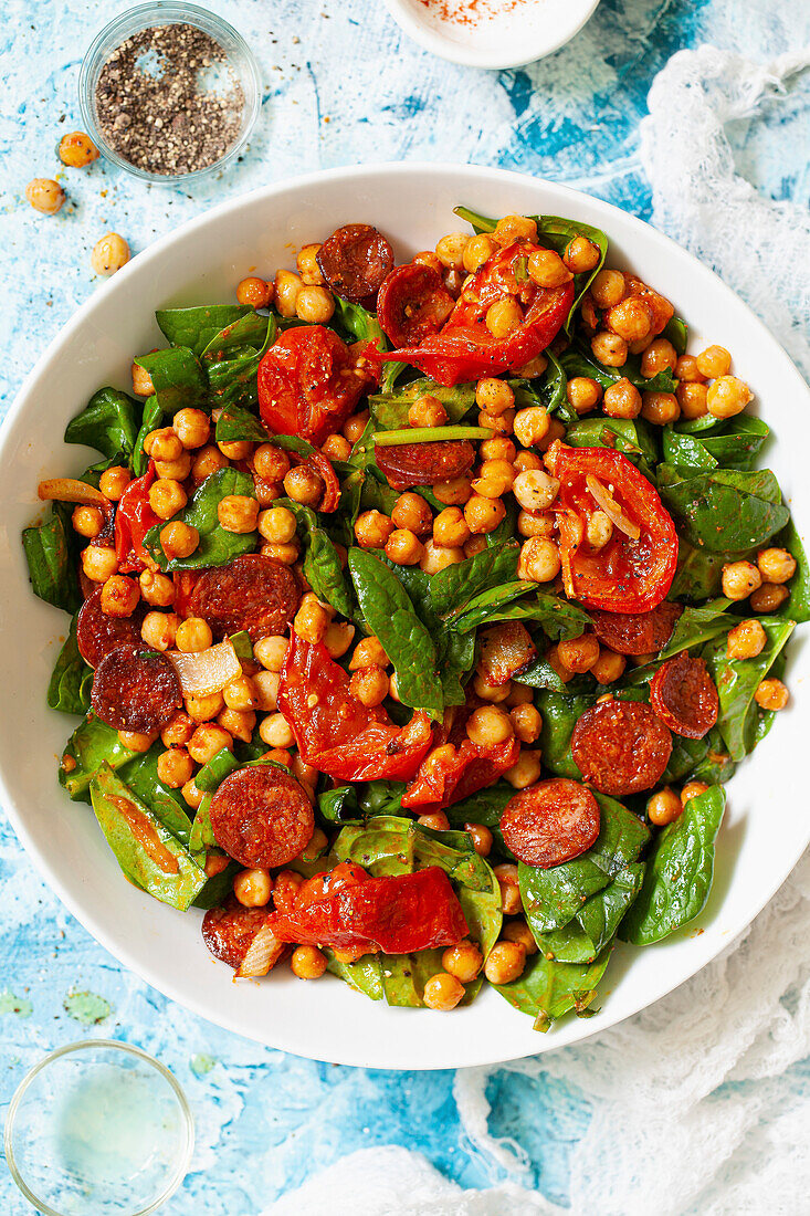 A bowl of roasted chickpea salad with spinach leaves, roasted tomatoes and fried chorizo.