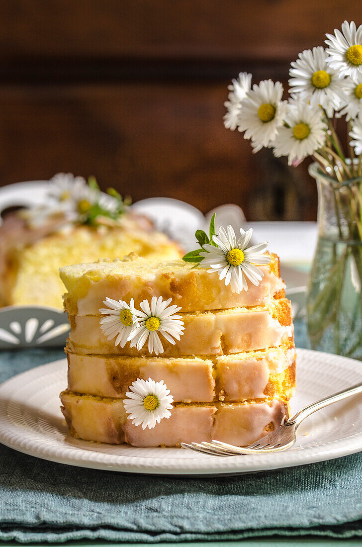 Lemon pound cake on a plate, on a table with daisies in a vase