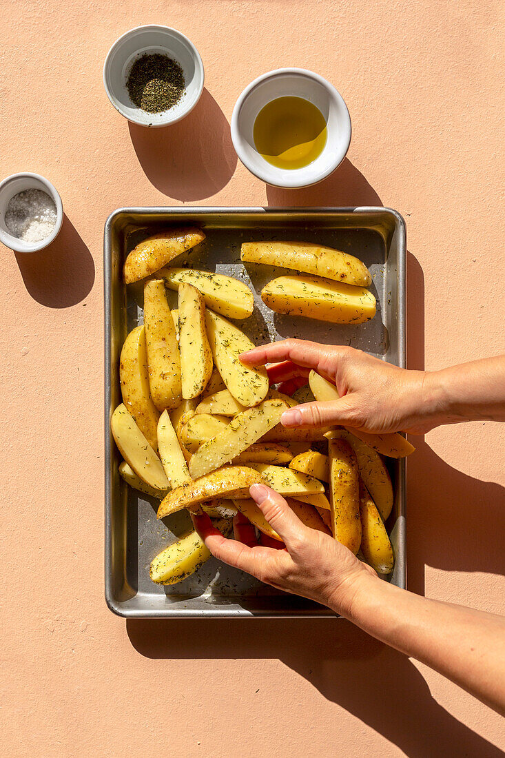 Geschnittene rohe Kartoffelspalten mit Salz, Olivenöl und getrockneten Kräutern mischen