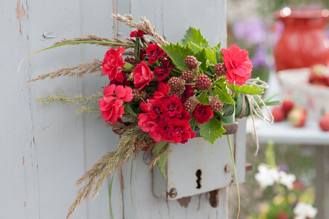 Red bouquet on door handle: carnation blossoms, unripe blackberries and grass blossoms
