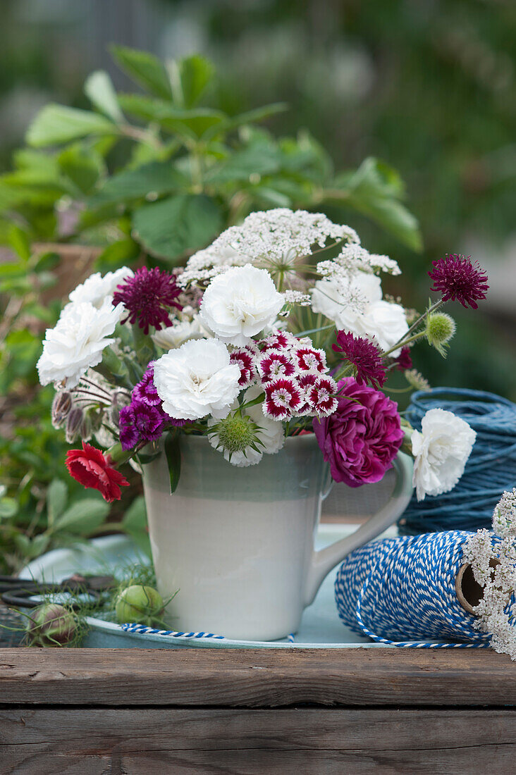 Strauß aus Rosenblüte, Nelken, Witwenblumen und wilder Möhre in Kaffeetasse