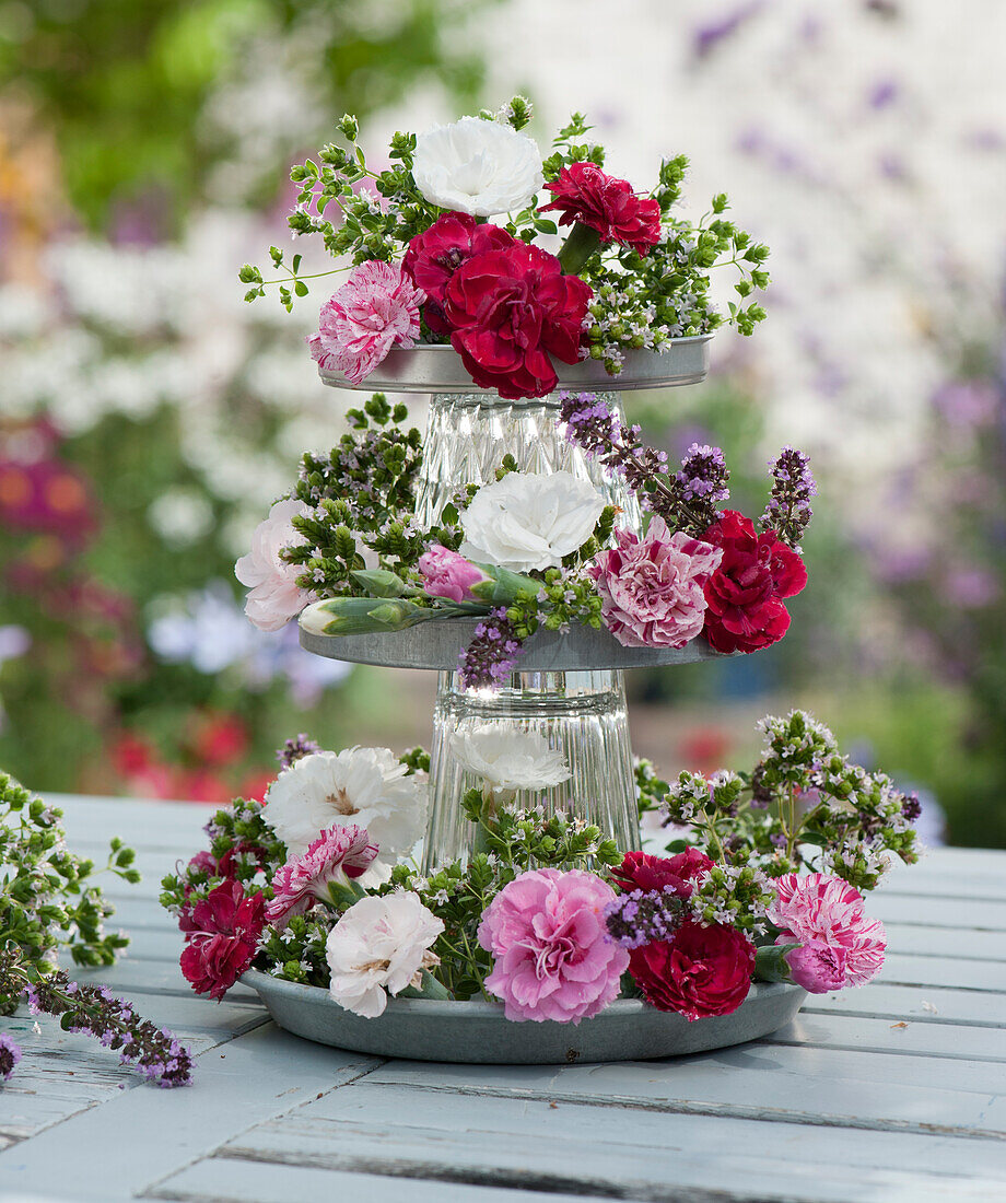 Handmade cupcake stand made of zinc coasters and glasses as fragrant table decoration with carnation blossoms and oregano blossoms