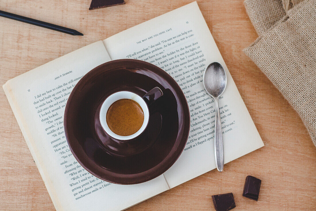 A cup of espresso on a book with a spoon and chocolate
