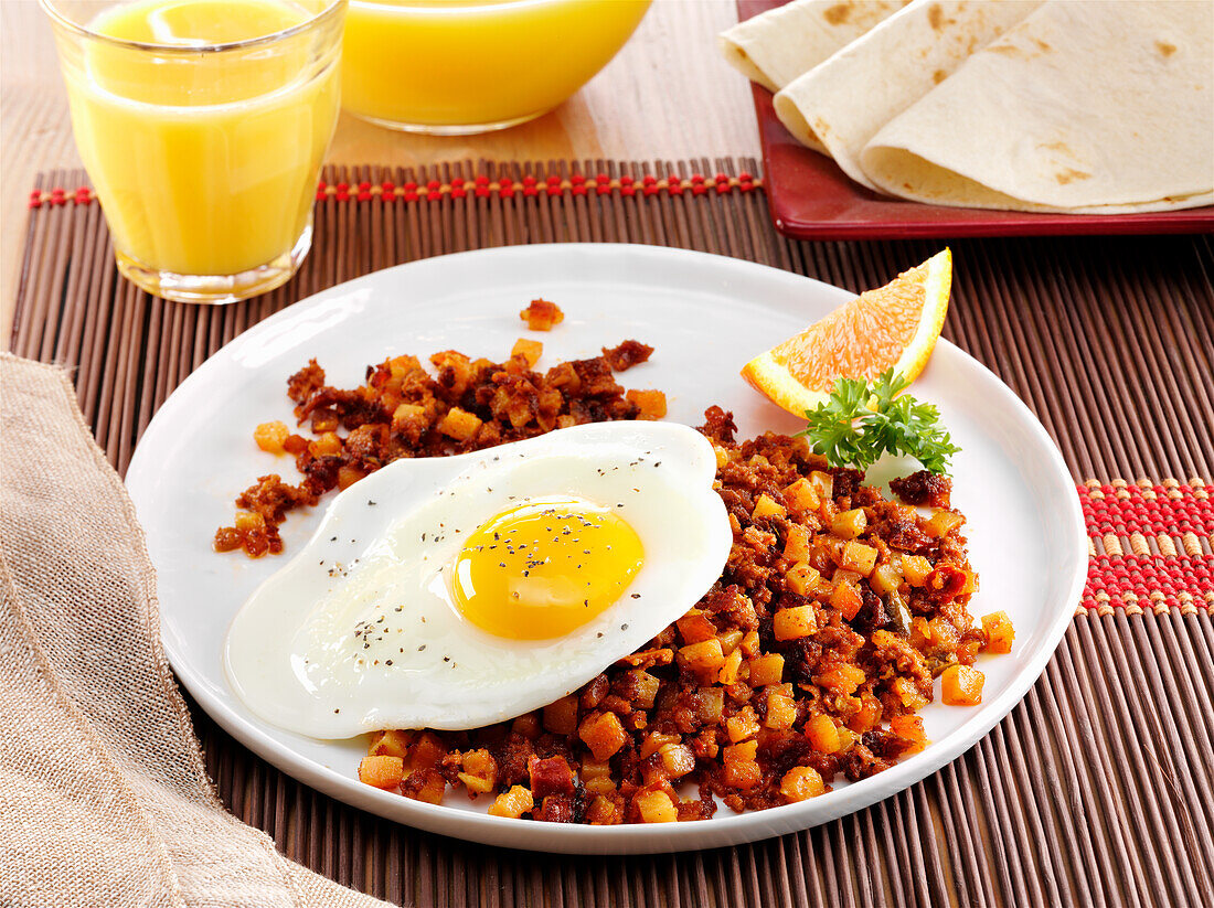 Mexican Chorizo hash topped with a fried egg and garnished with a wedge of orange