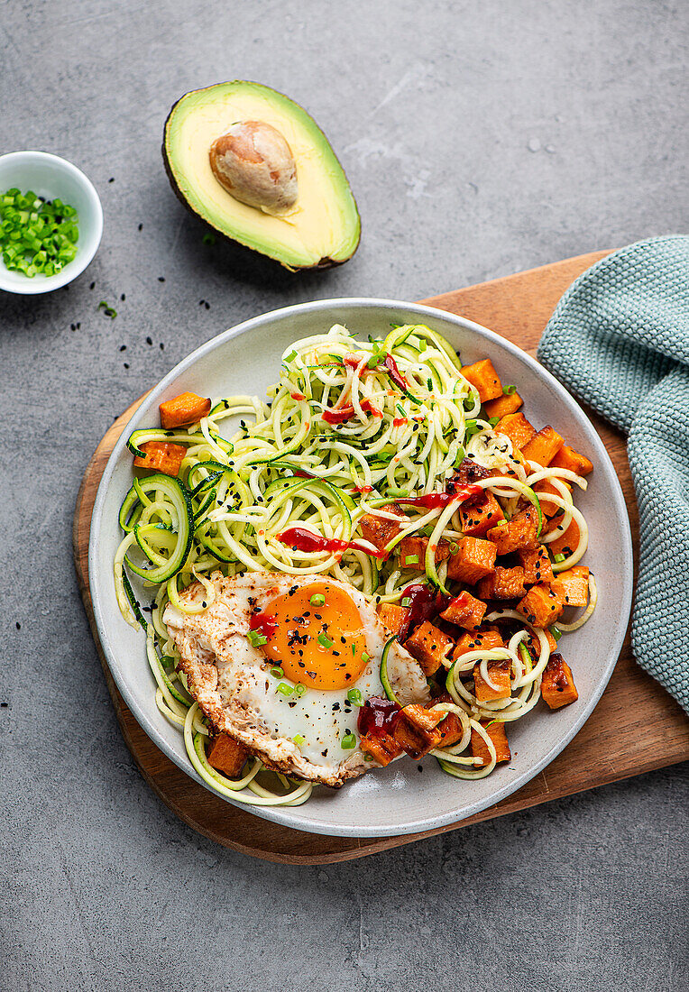 A breakfast bowl with zoodles, sweet potatoes, fried egg and ketchup