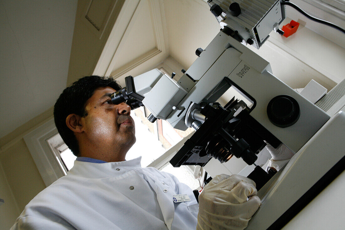 Pathologist analysing a sample under a microscope.