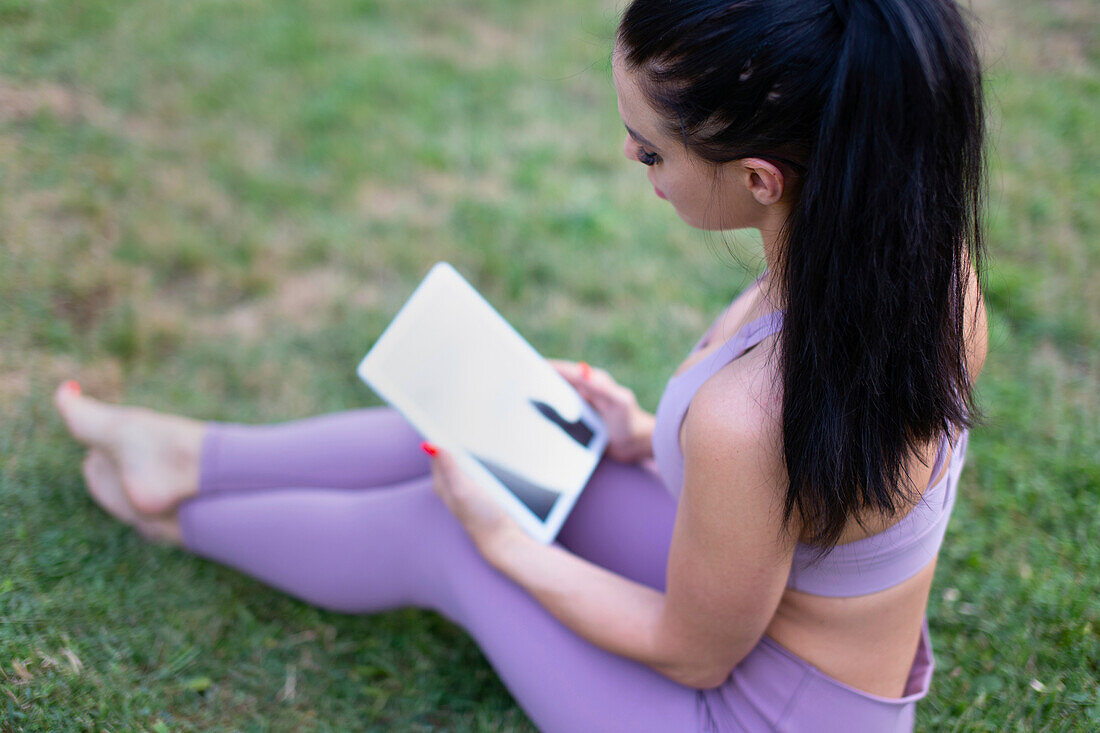 Young woman using digital tablet sitting on grass