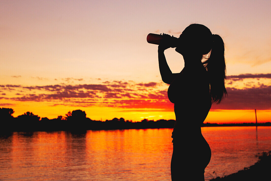 Silhouette of a woman drinking from a bottle