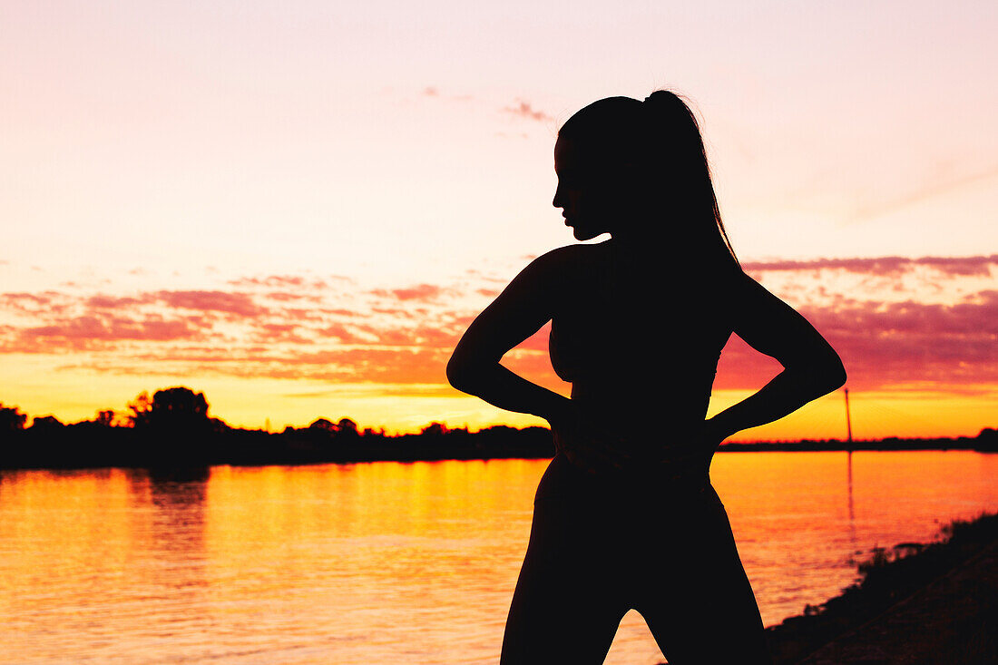 Silhouette of a woman in golden sunset at riverbank