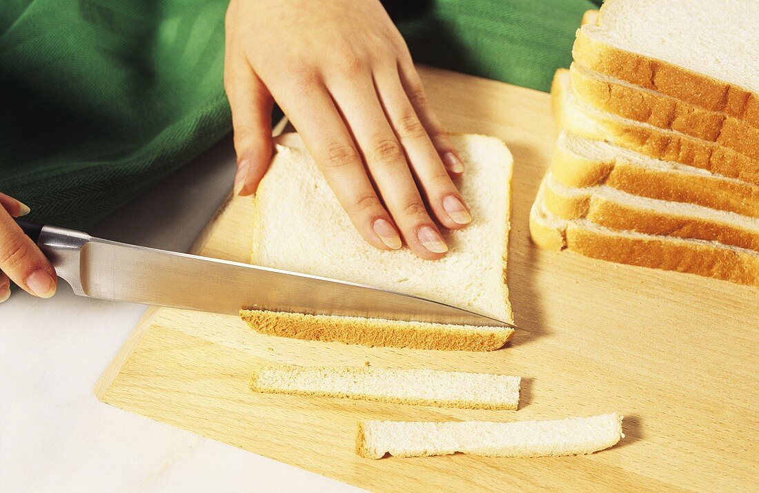 Cutting the crusts off slices of white bread for sandwiches