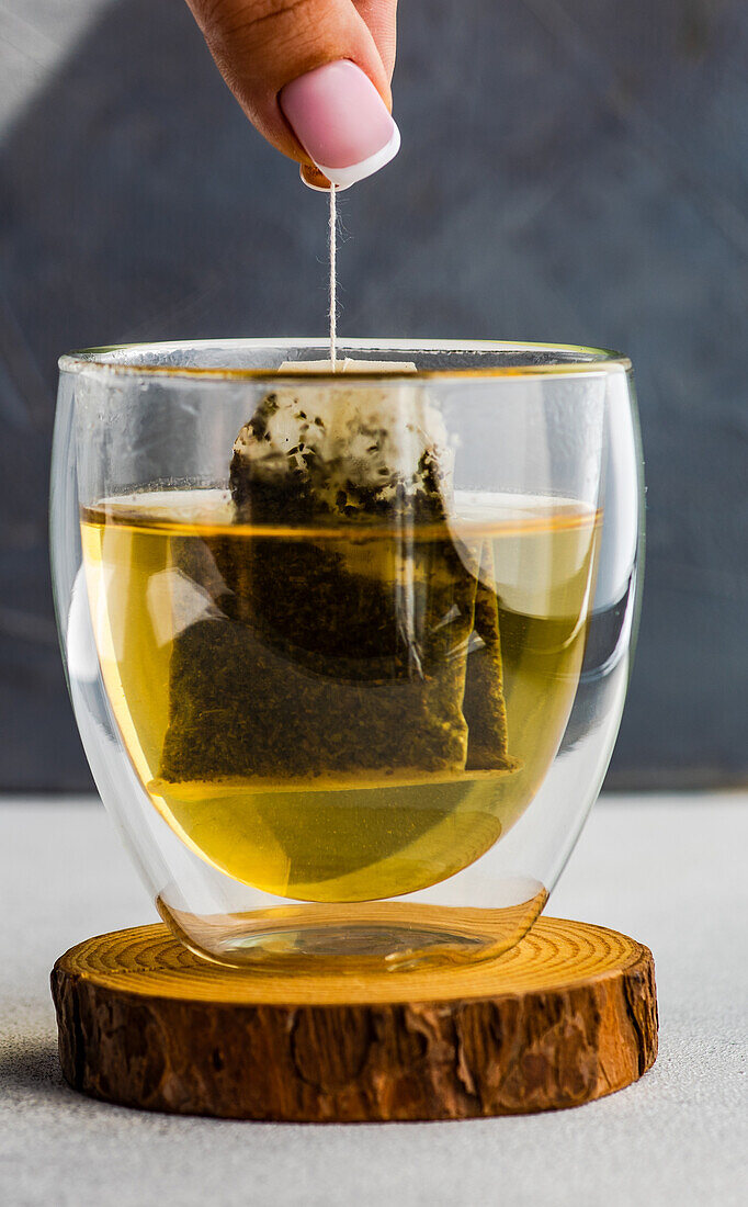 Woman hands hold of green tea bag in double glass cup