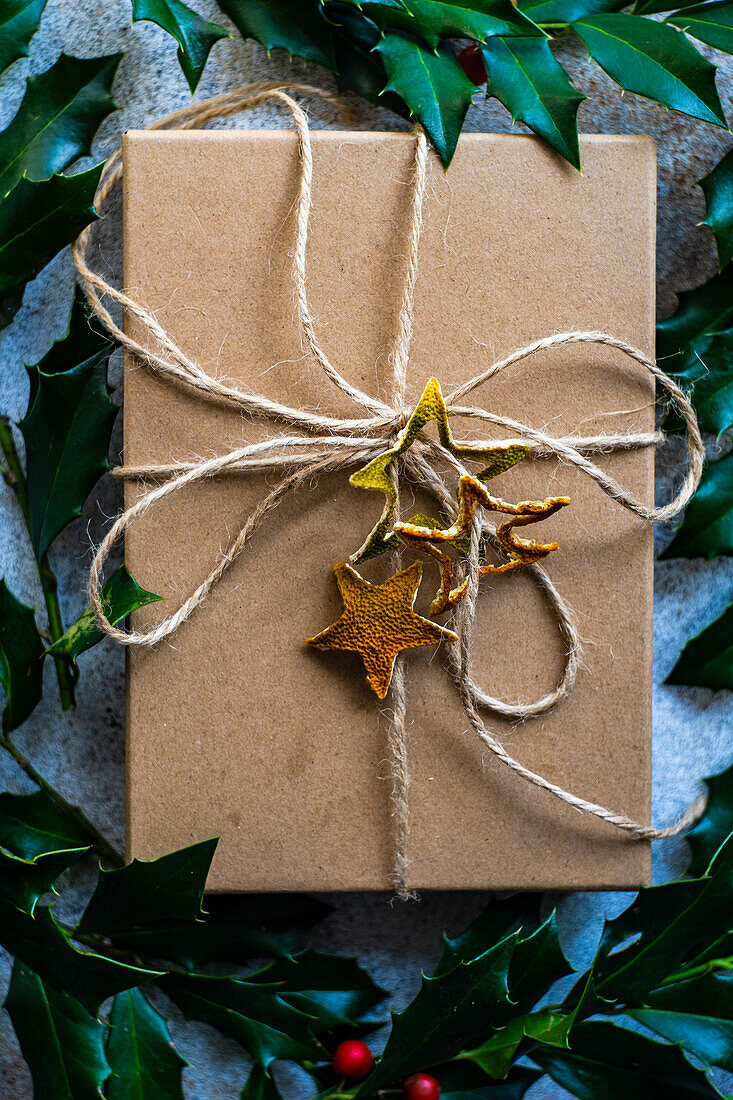 Rustic gift box decorated with fresh holly berry plant on concrete background