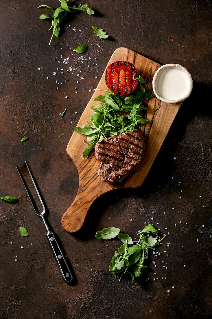 Grilled beef steak served with creamy sauce, grilled vegetables tomato and arugula salad