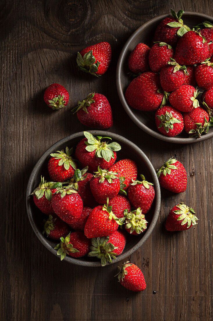 Strawberries in dark bowls on wood background
