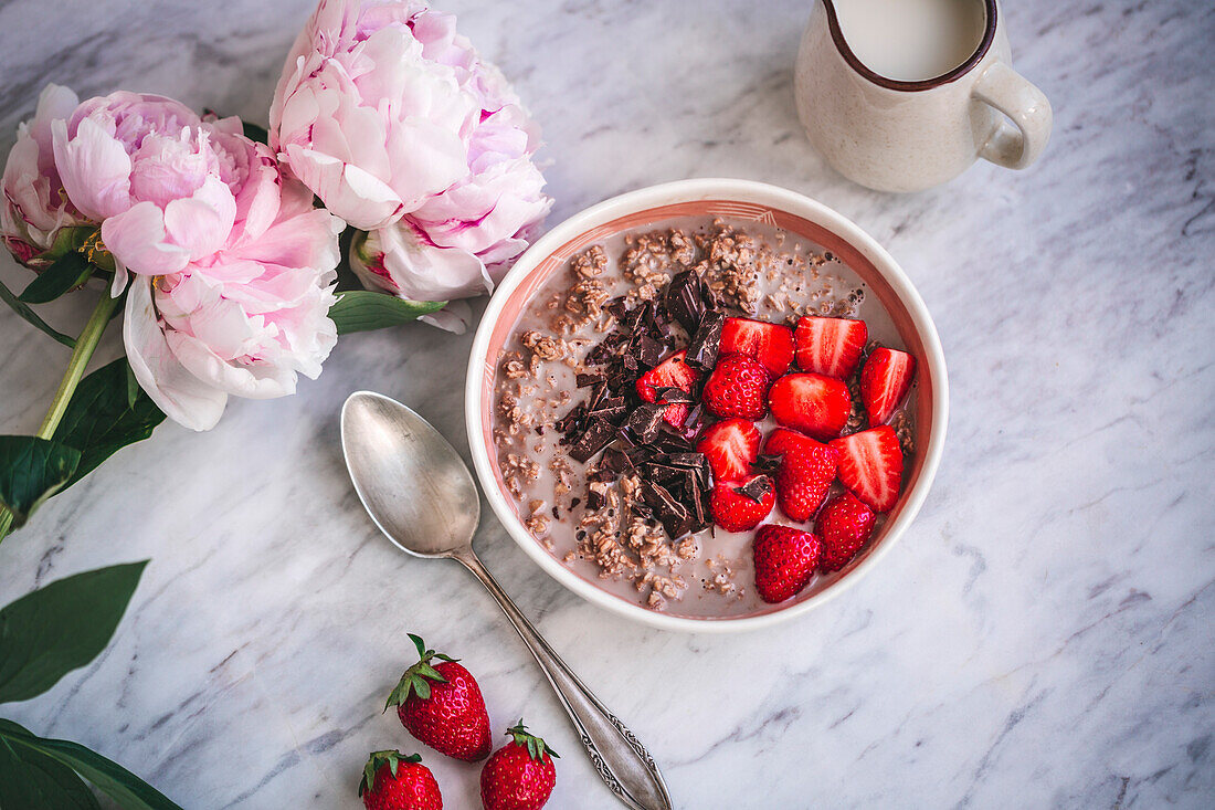 Oats with strawberries and dark chocolate on a marble background, with flowers