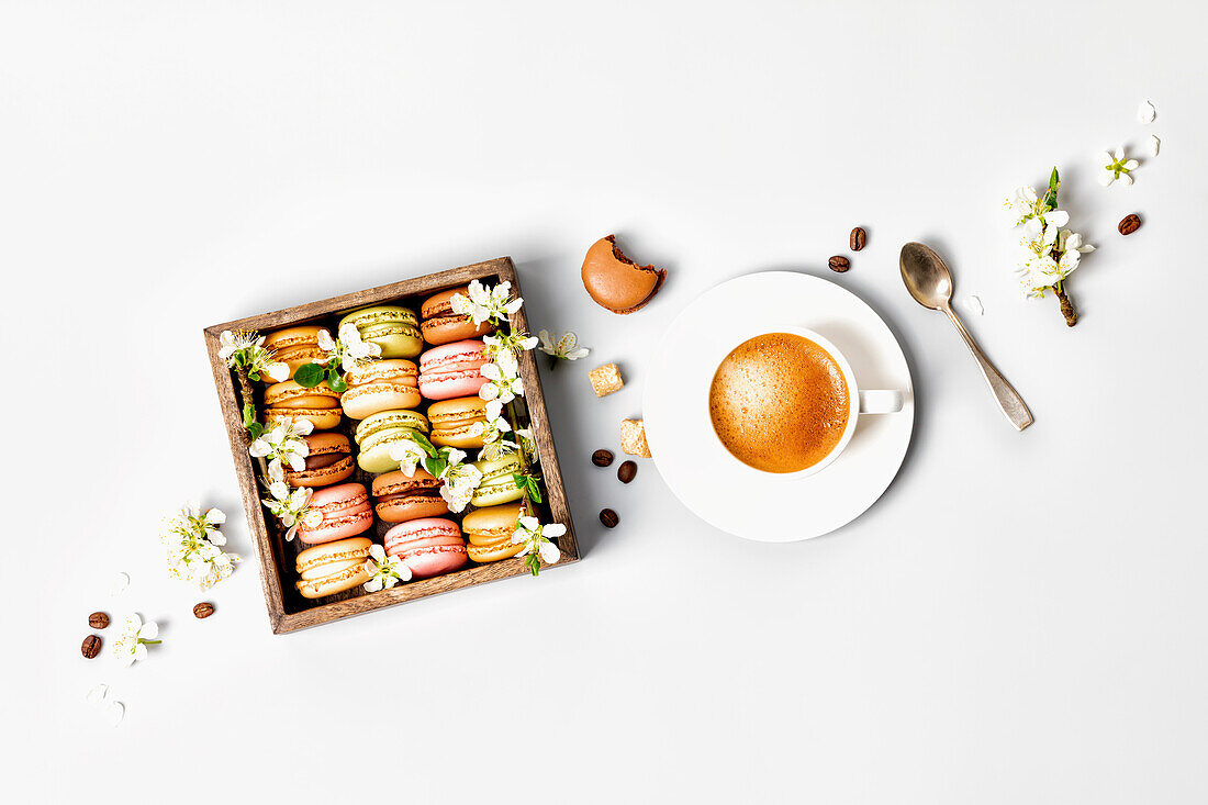Verschiedene Macarons in Holzkiste mit Frühlingsblüten daneben eine Tasse Kaffee