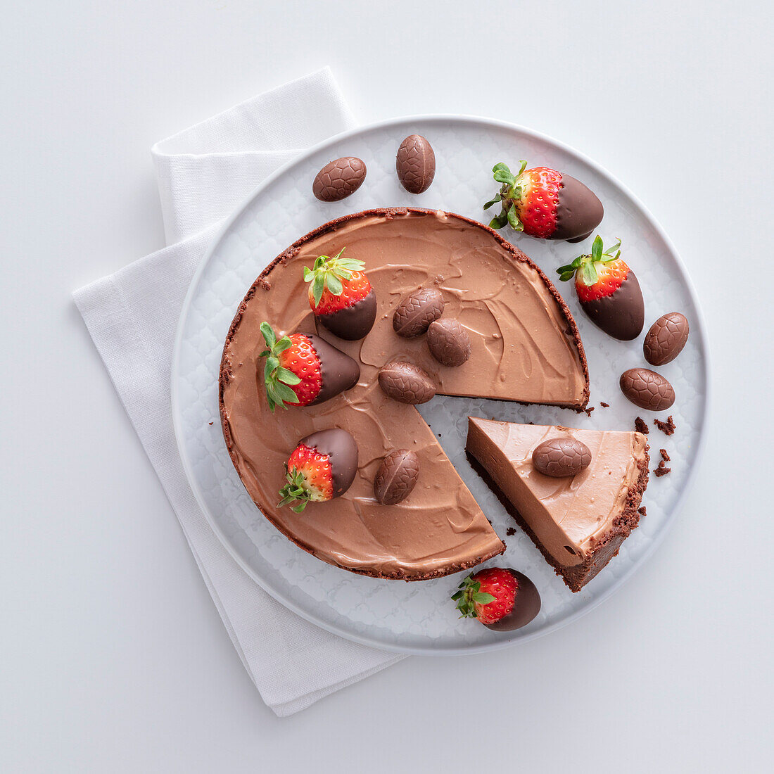 A slice being taken out of a Chocolate cheesecake with chocolate-dipped strawberries