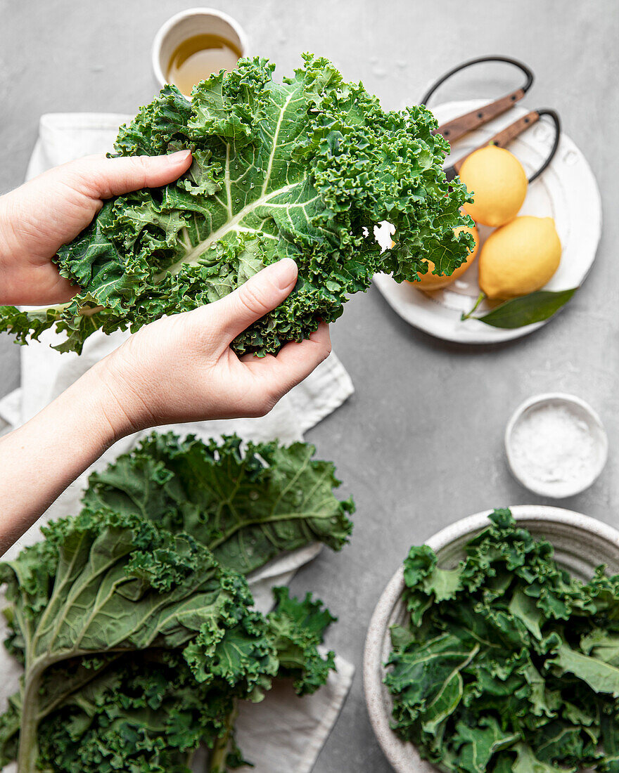 Hands holding a bright green, freshly washed curly kale leaf