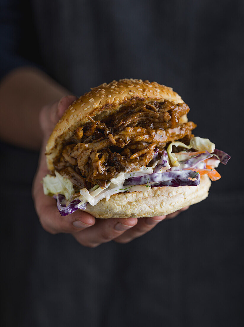 Dry Rubbed and Smoked Pulled Pork Burger being held in a persons hand