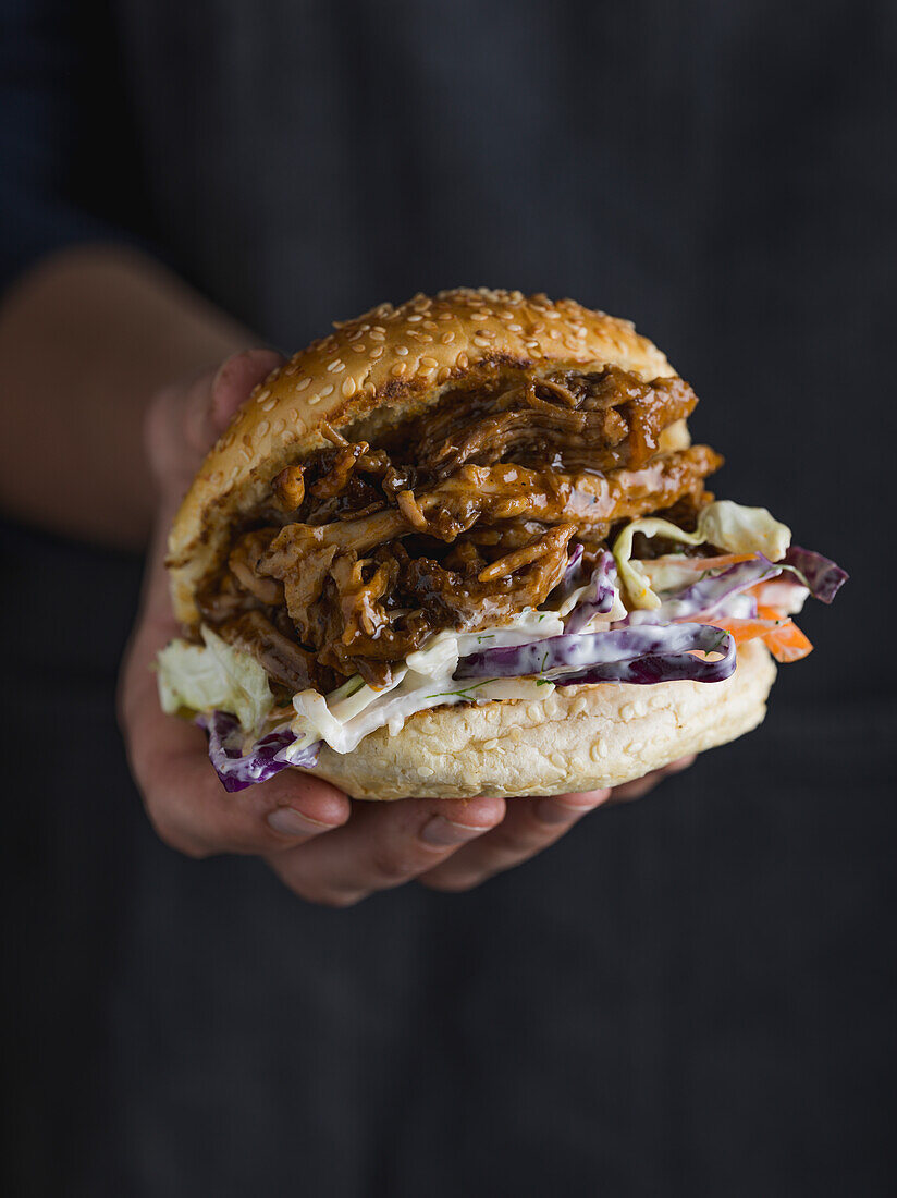 Hand hält Pulled Pork Burger, dry rubbed und geräuchert