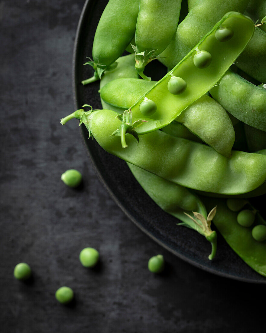 Snap peas in a black bowl on a dark surface
