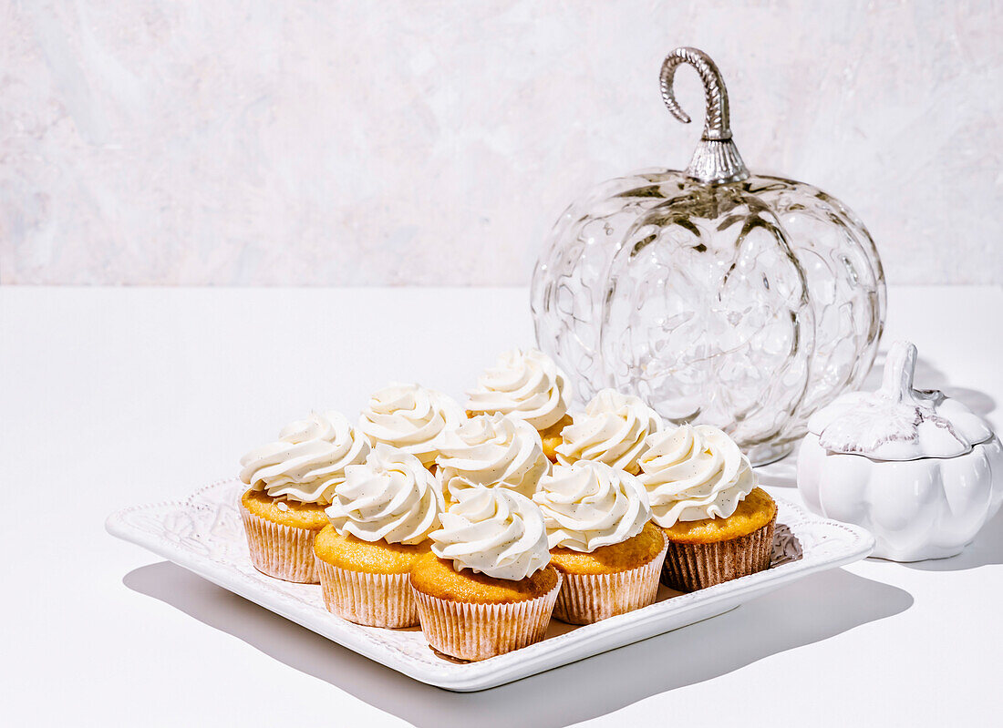Vanille-Cupcakes und kürbisförmige Dekoobjekte