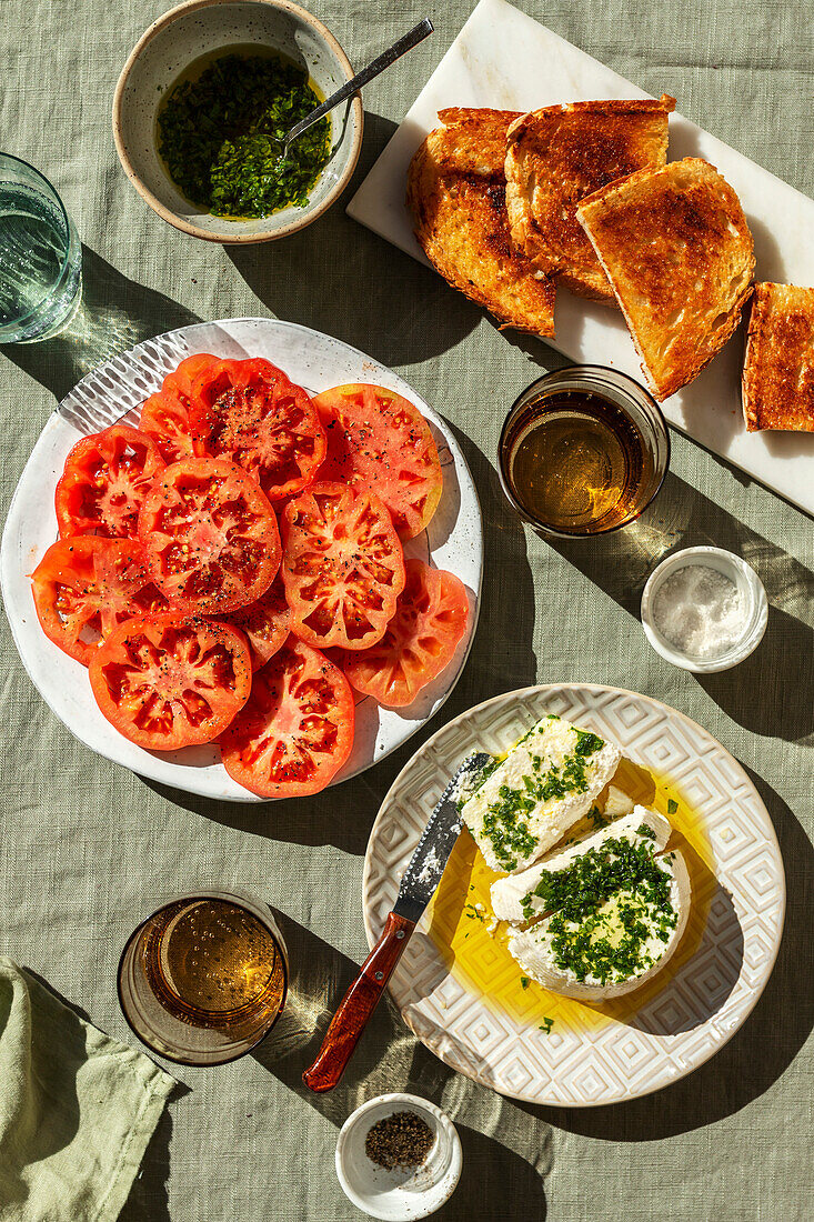 Sliced tomato on a plate and ricotta cheese, salsa dressing and bread toasts on the side
