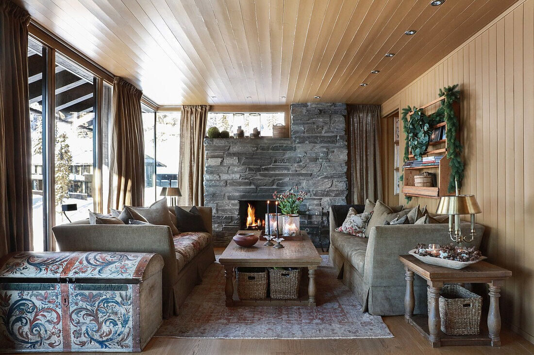 Klassisches Wohnzimmer mit Kamin und Holzverkleidung in einer Hütte, bemalte Holztruhe im Vordergrund