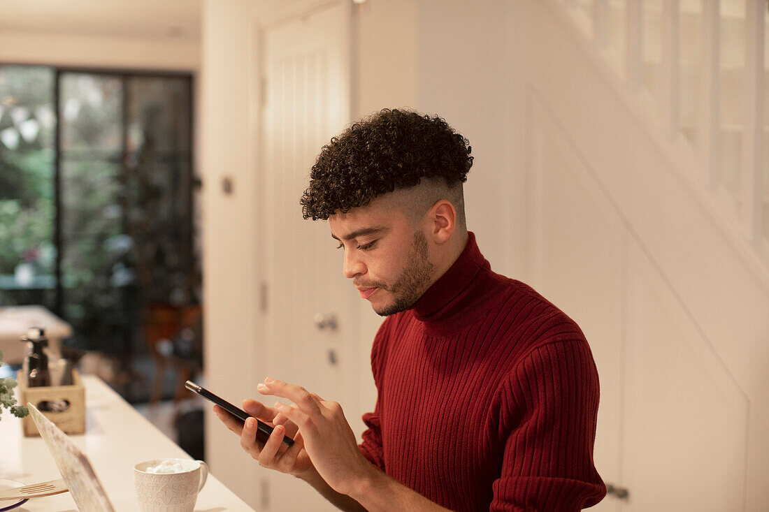 Young man using smart phone in kitchen