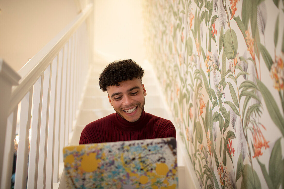 Happy young man using laptop on staircase