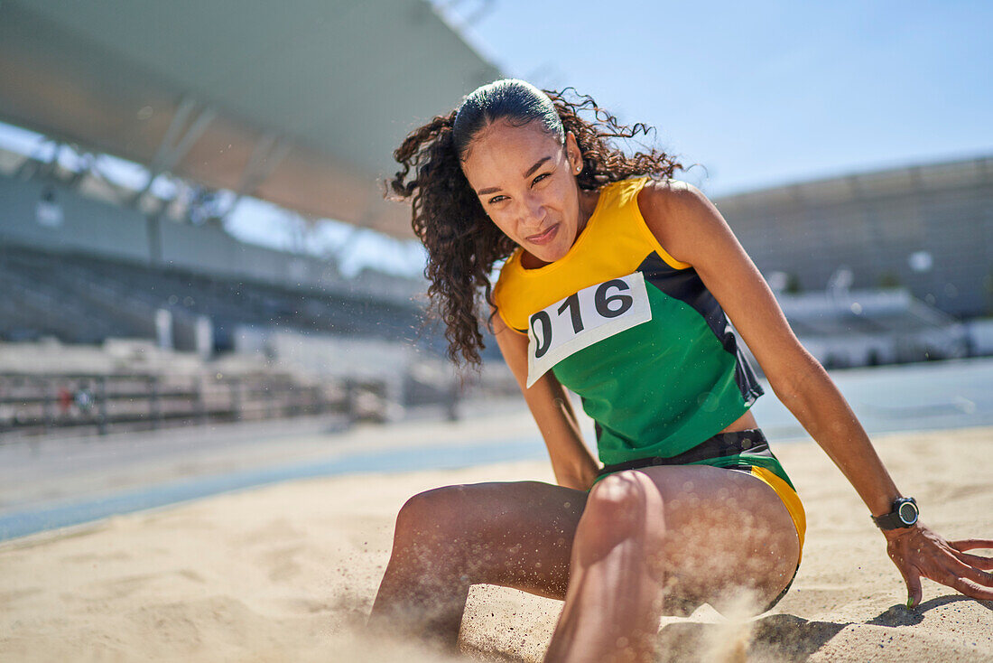 Female track and field athlete long jumping in sand