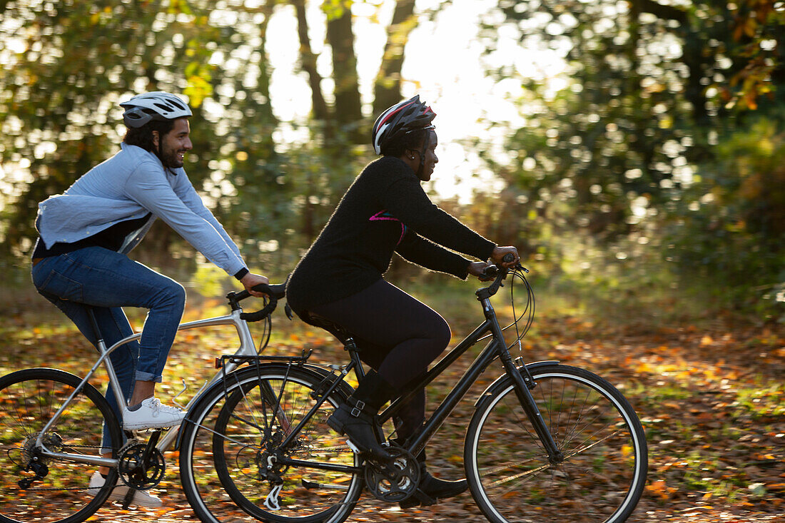 Friends riding bicycles through autumn leaves in park