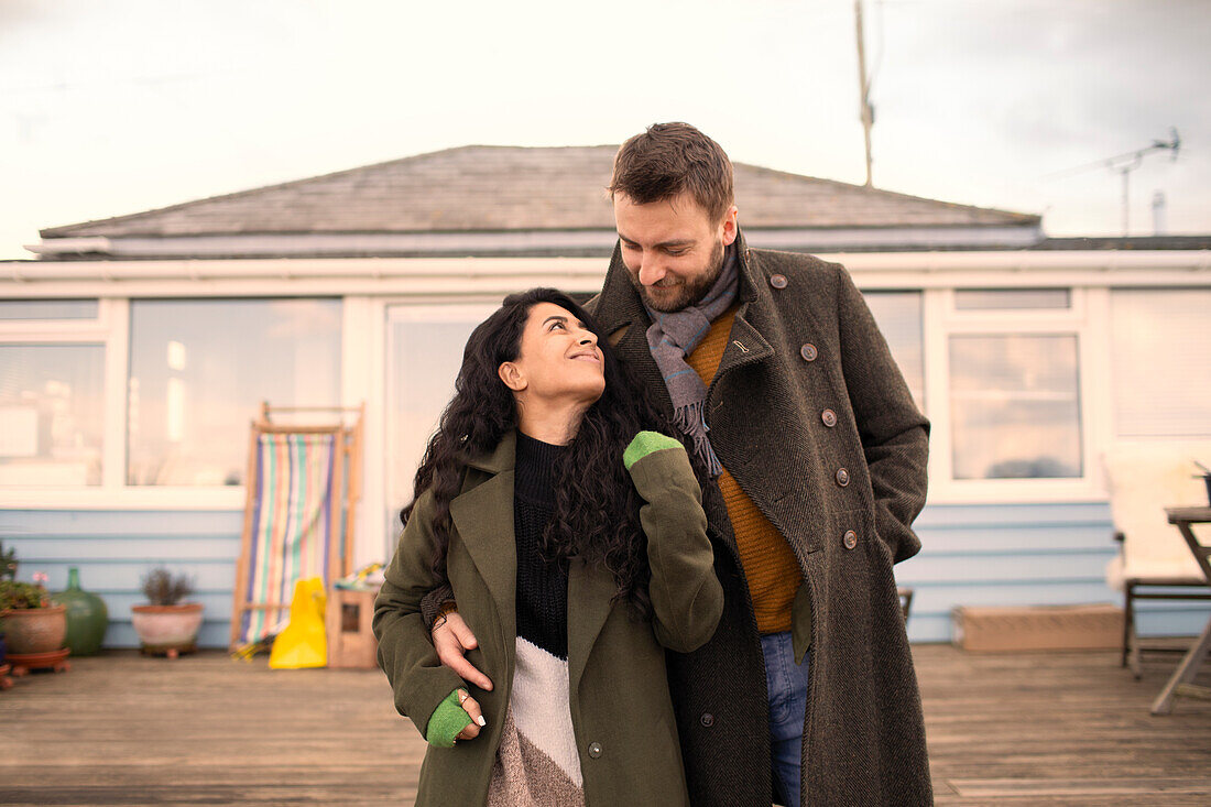 Happy couple in winter coats hugging outside house