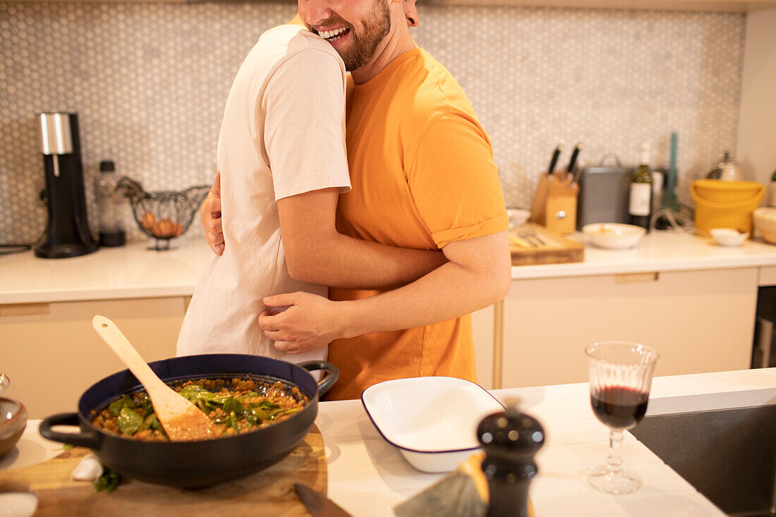 Happy gay male couple cooking and hugging in kitchen