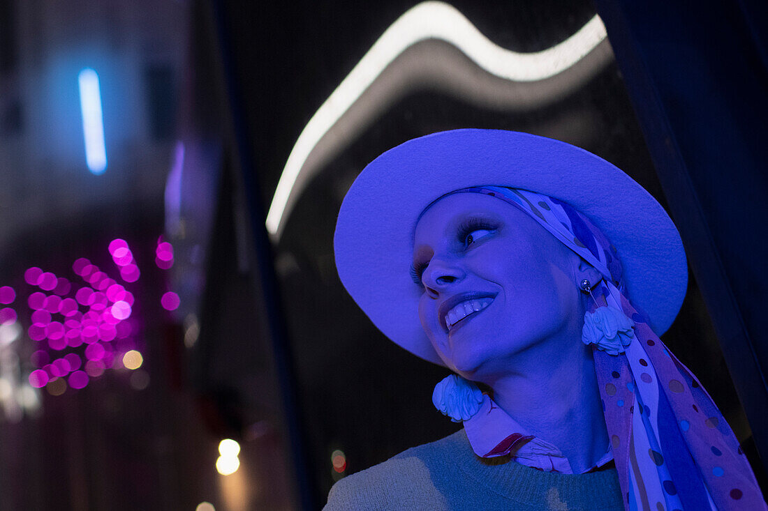 Happy woman in fedora under neon lights