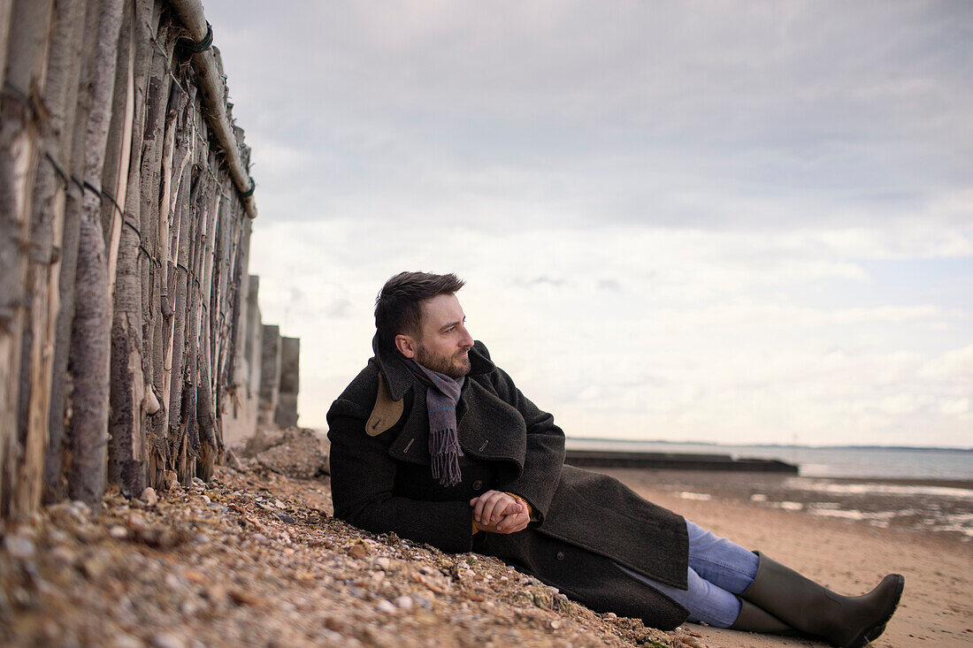 Serene man in winter coat relaxing on beach