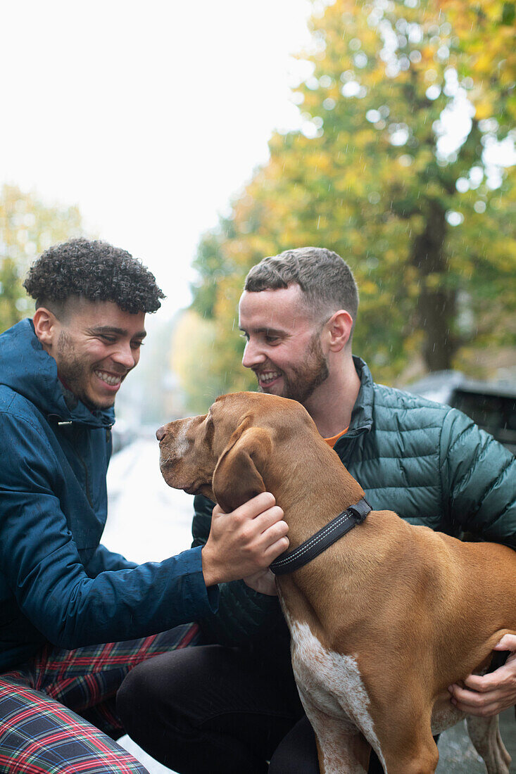 Happy gay male couple petting dog on street